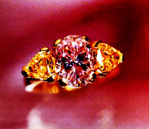 A 3-carat fancy orangy pink diamond flanked by two fancy yellow trilliants.